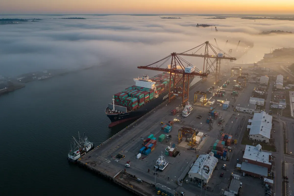 A large container ship docks at the Avoyelles Port Commission cranes extend over a busy waterfront scene