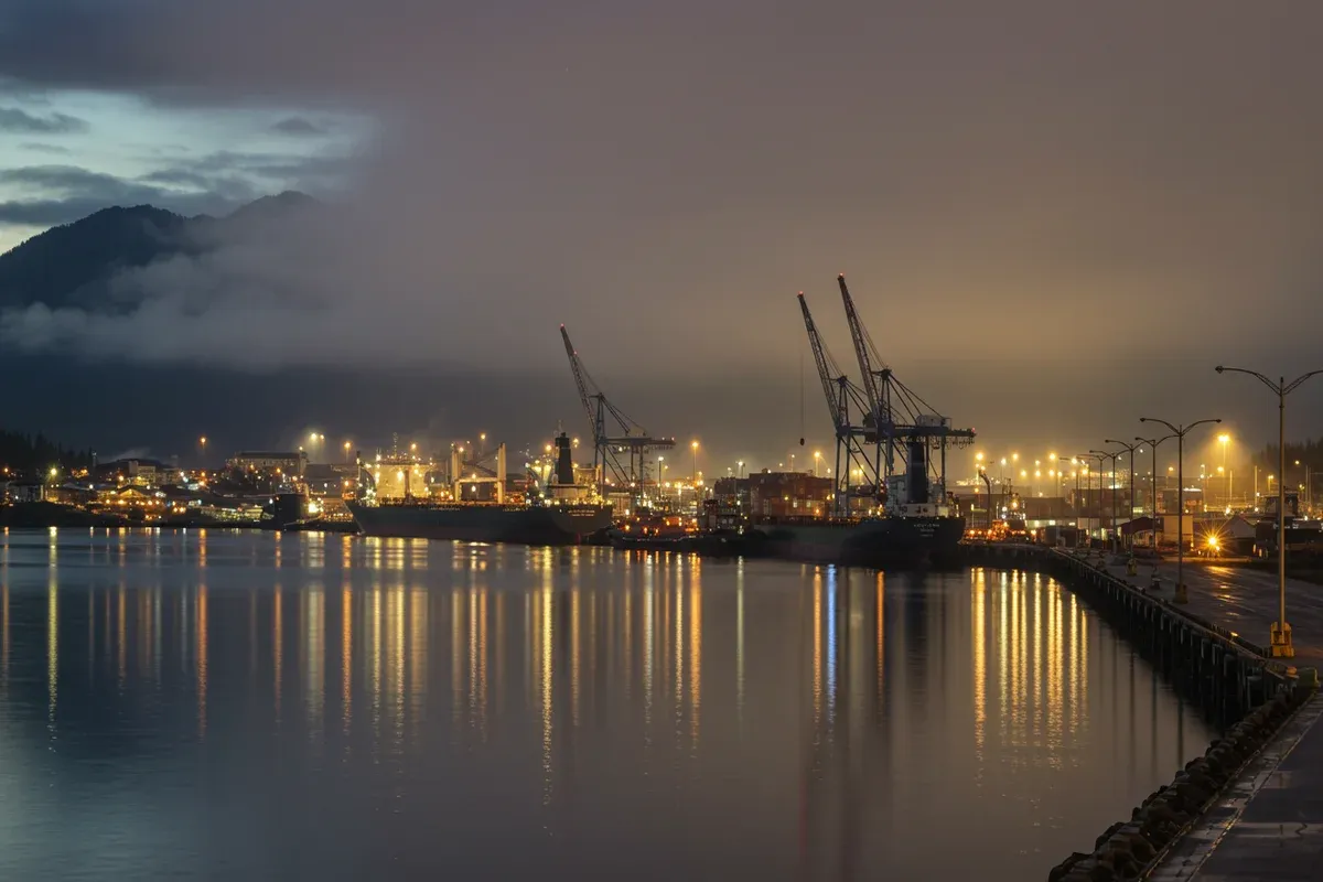 Reflections of tall cranes illuminate a calm harbor in Kodiak City Alaska vibrant lights shimmer on the water surface