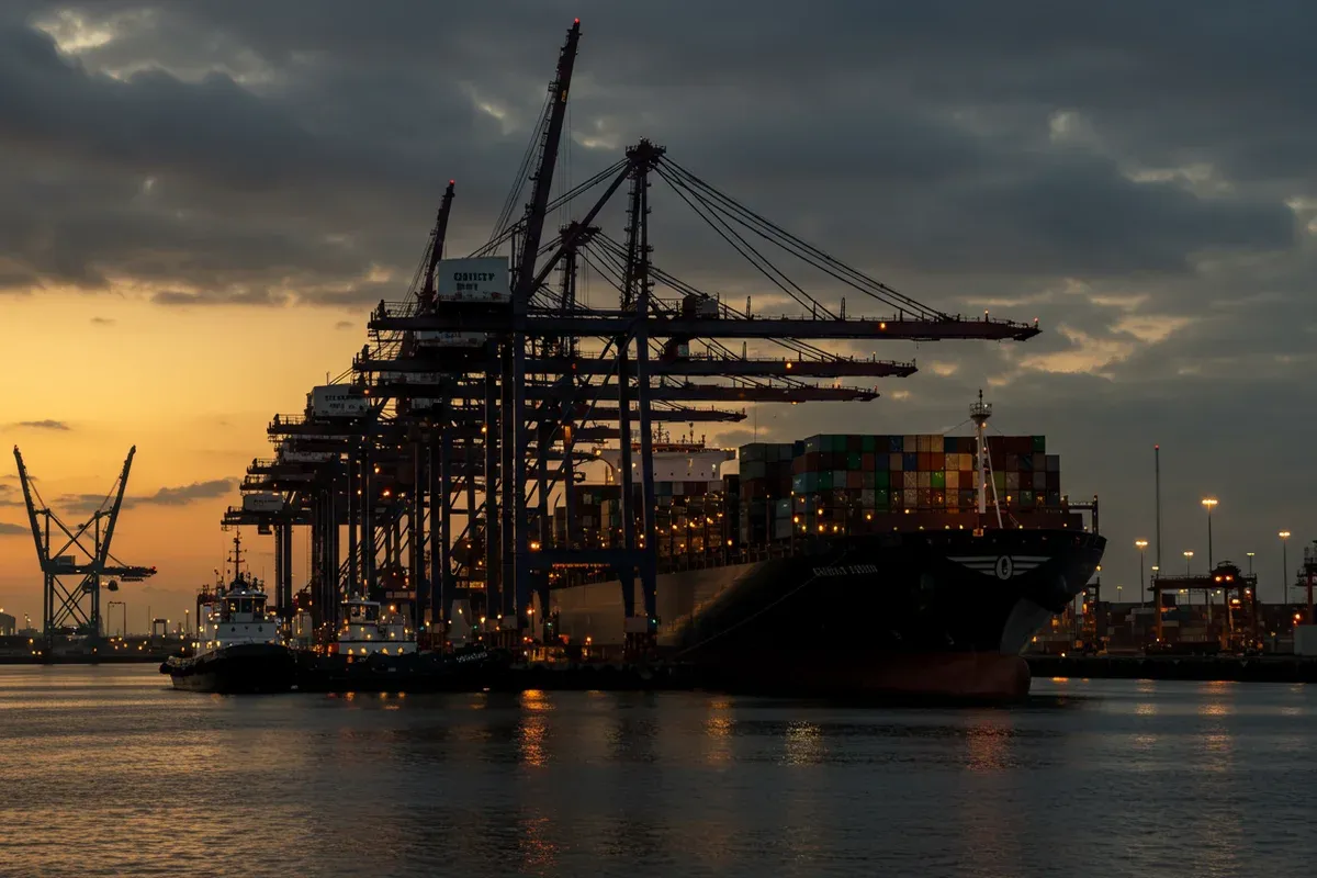 A large cargo ship City of Saint Louis sits in a harbor filled with towering cranes and illuminated by city lights