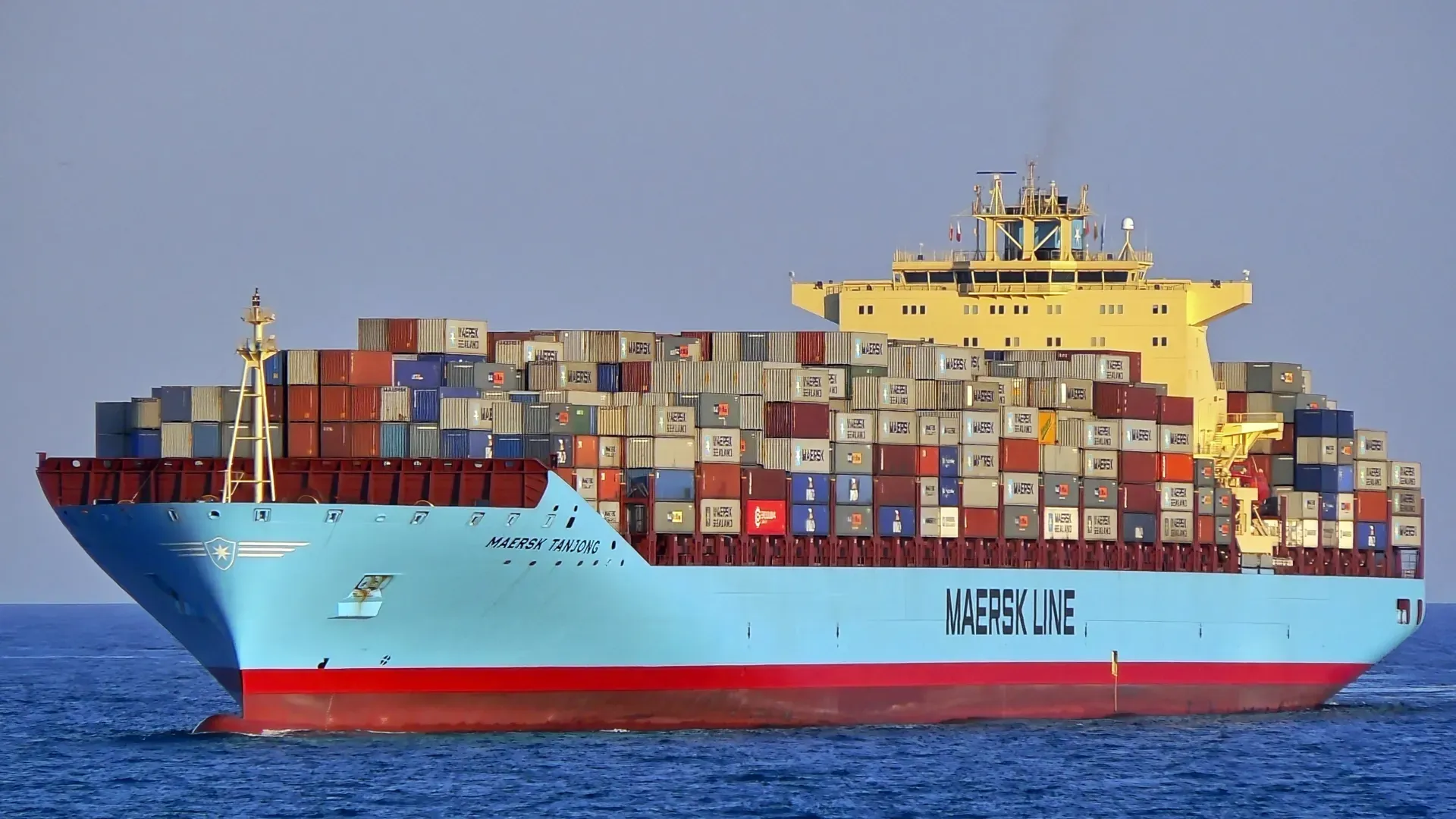 A Maersk Line container ship navigates the ocean with a towering smokestack and numerous cargo containers onboard