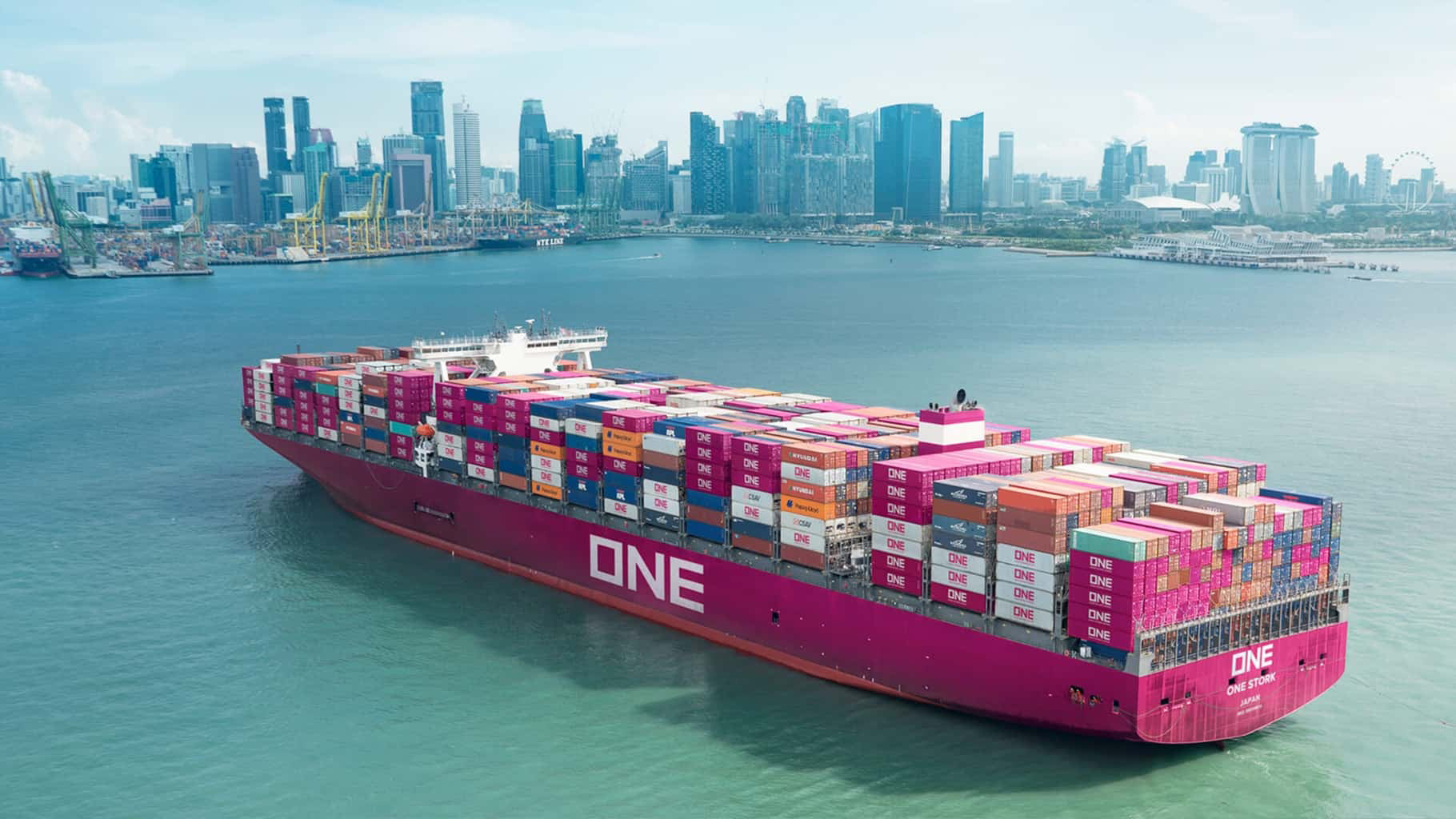 A vibrant pink container ship navigates through the harbor with a skyline of Singapore buildings in the background