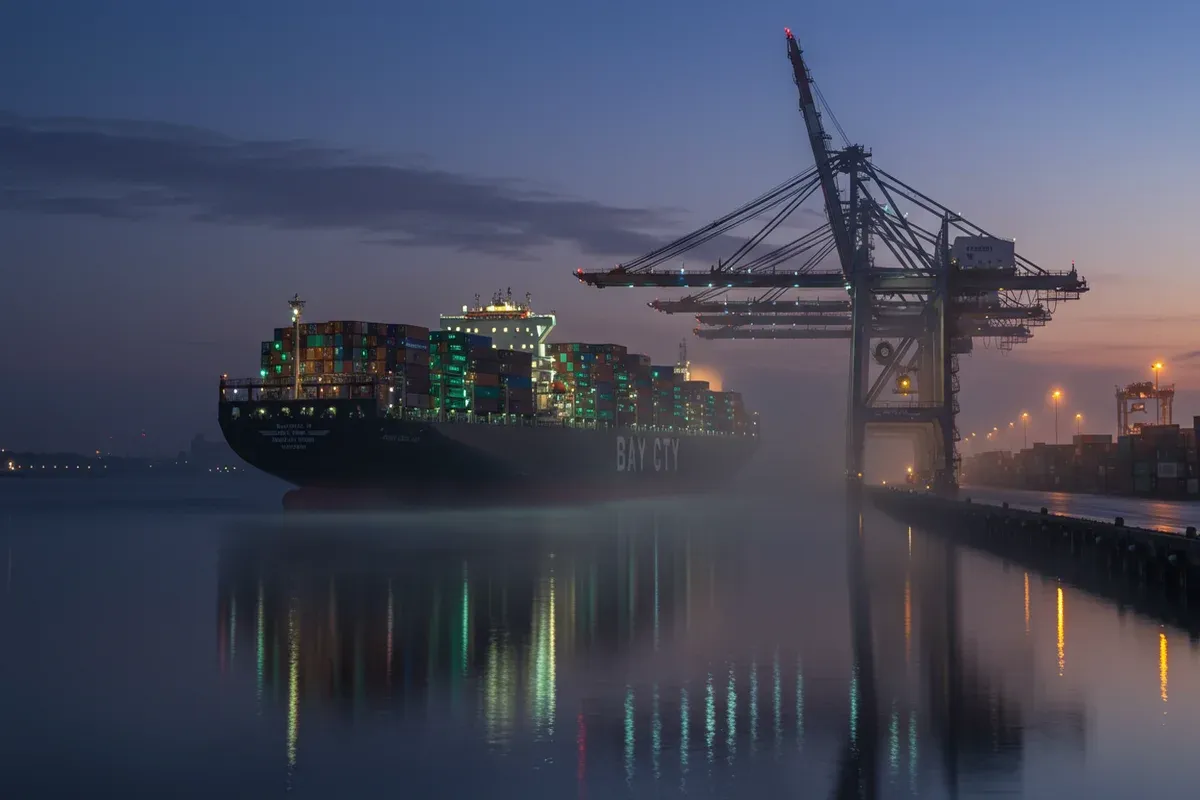 A dark freighter reflects in the calm waters of Bay Citys harbor illuminated by city lights