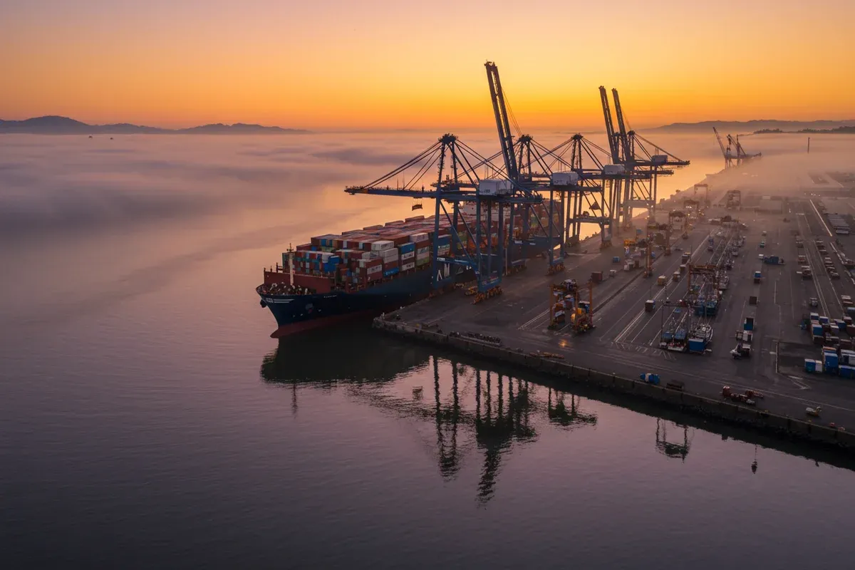 A massive cargo ship rests in Richmond Channel reflecting the city skyline and palm trees during a hazy sunset
