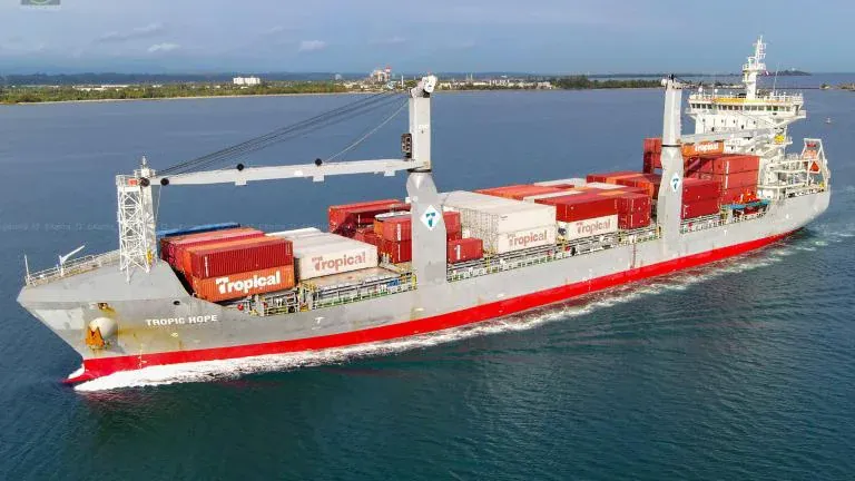 A large container ship navigates the ocean with visible cargo containers and a prominent superstructure