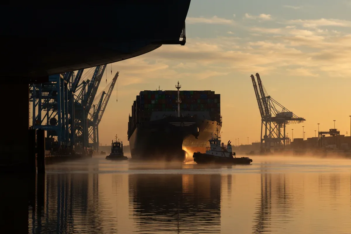 A ship navigates the misty Upper Mississippi River Basin with tugboats assisting its passage reflecting in the calm water