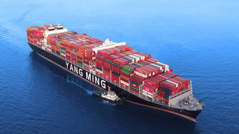 A large container ship the Yang Ming navigates the ocean with a prominent bow and superstructure under a blue sky