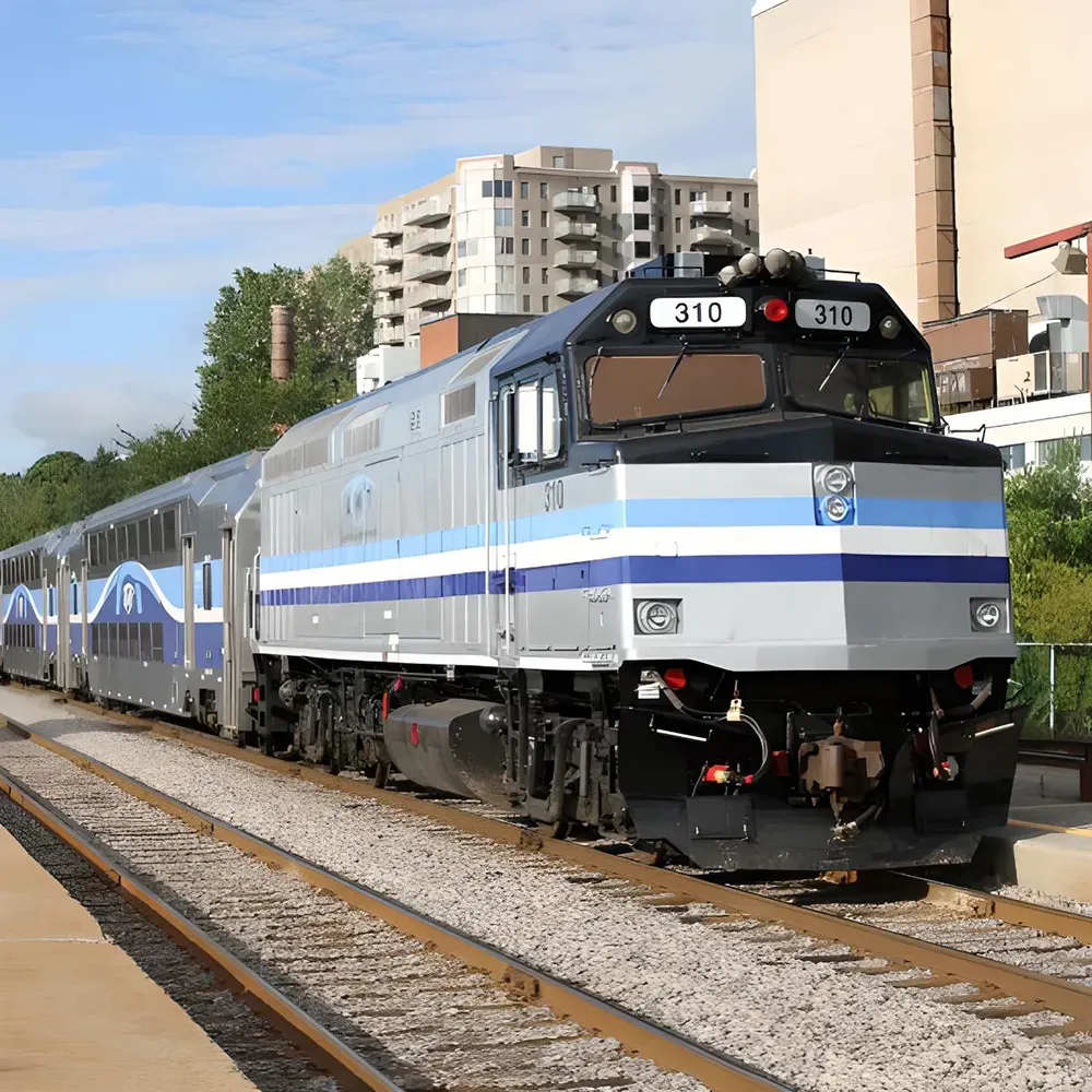 A gray AMT carrier train sits on a tracks adjacent to a building with blue stripes The train is detailed with windows and