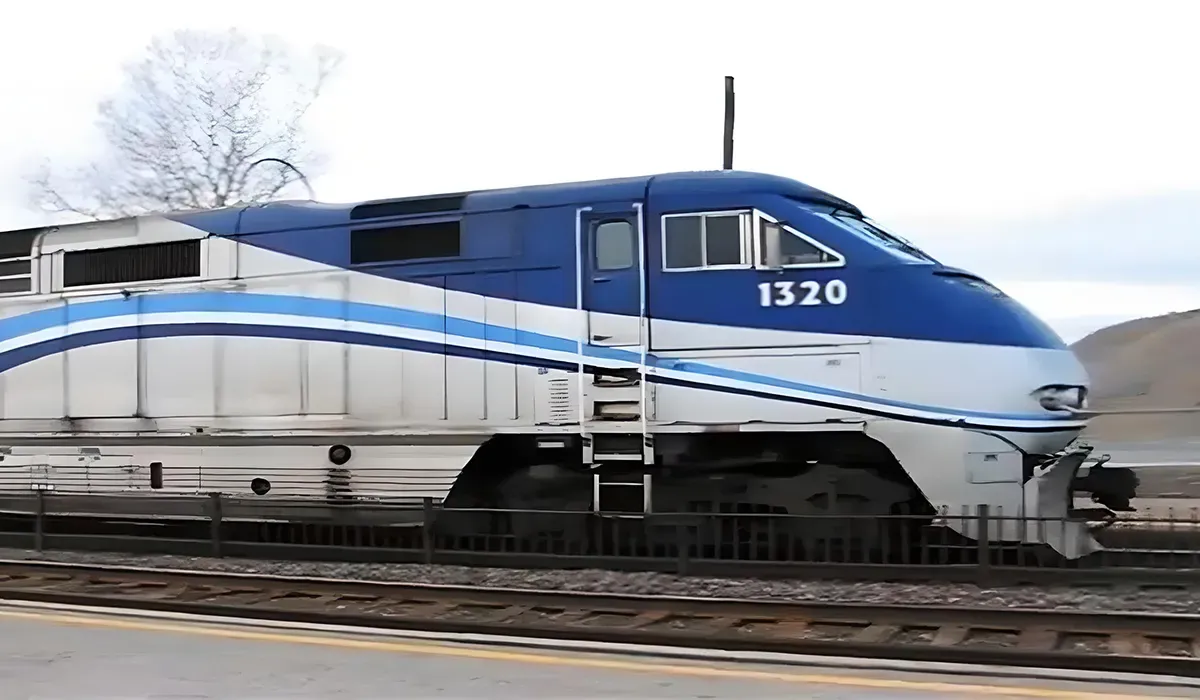 A sleek white Amtrak train speeds along a track with prominent blue accents and the number 1320 visible