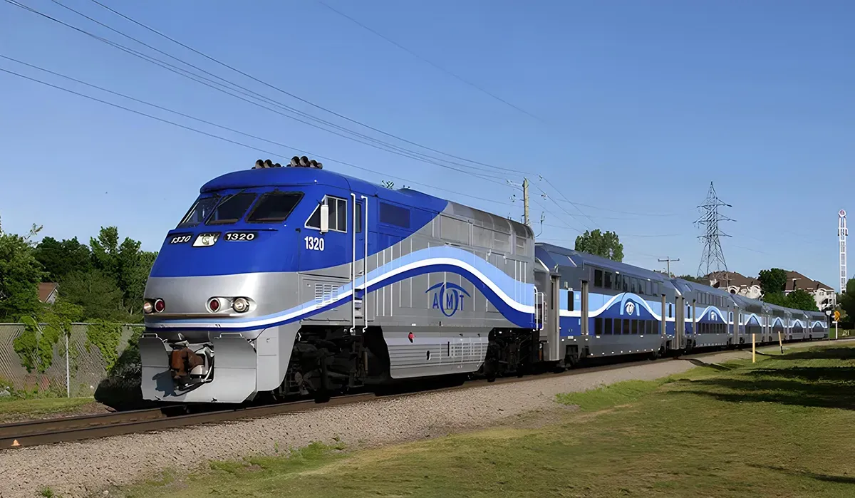 A blue and white AMT transit train moves along a city street with green trees lining the track It appears to be heading