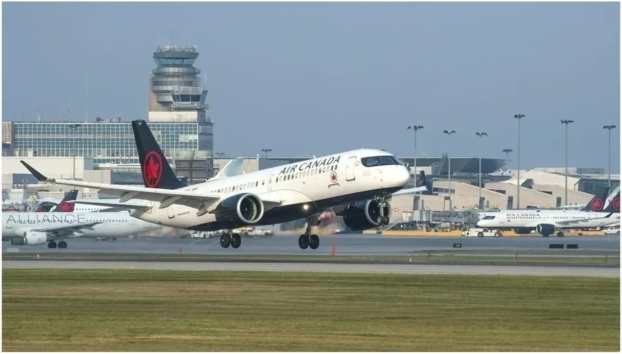 An Air Canada aircraft is in flight landing at an airport with a cityscape backdrop