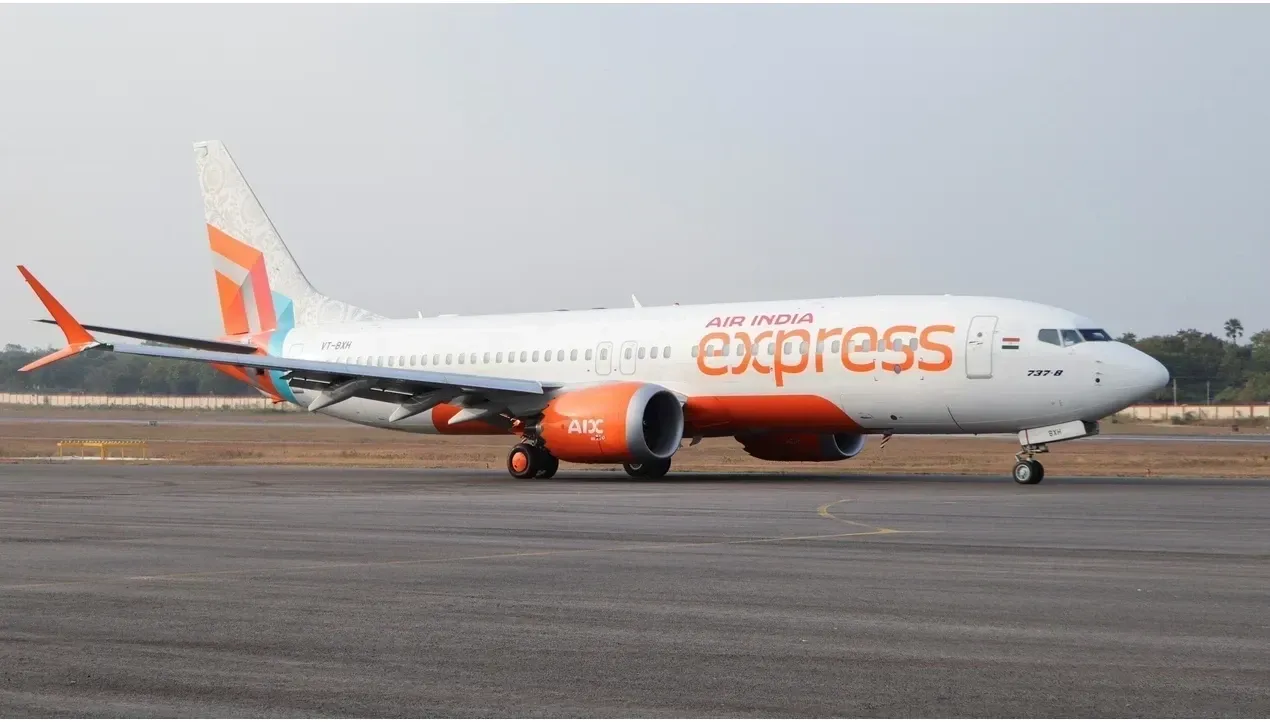 An Air India Express jet rests on the tarmac displaying a vibrant orange color scheme ready for flight