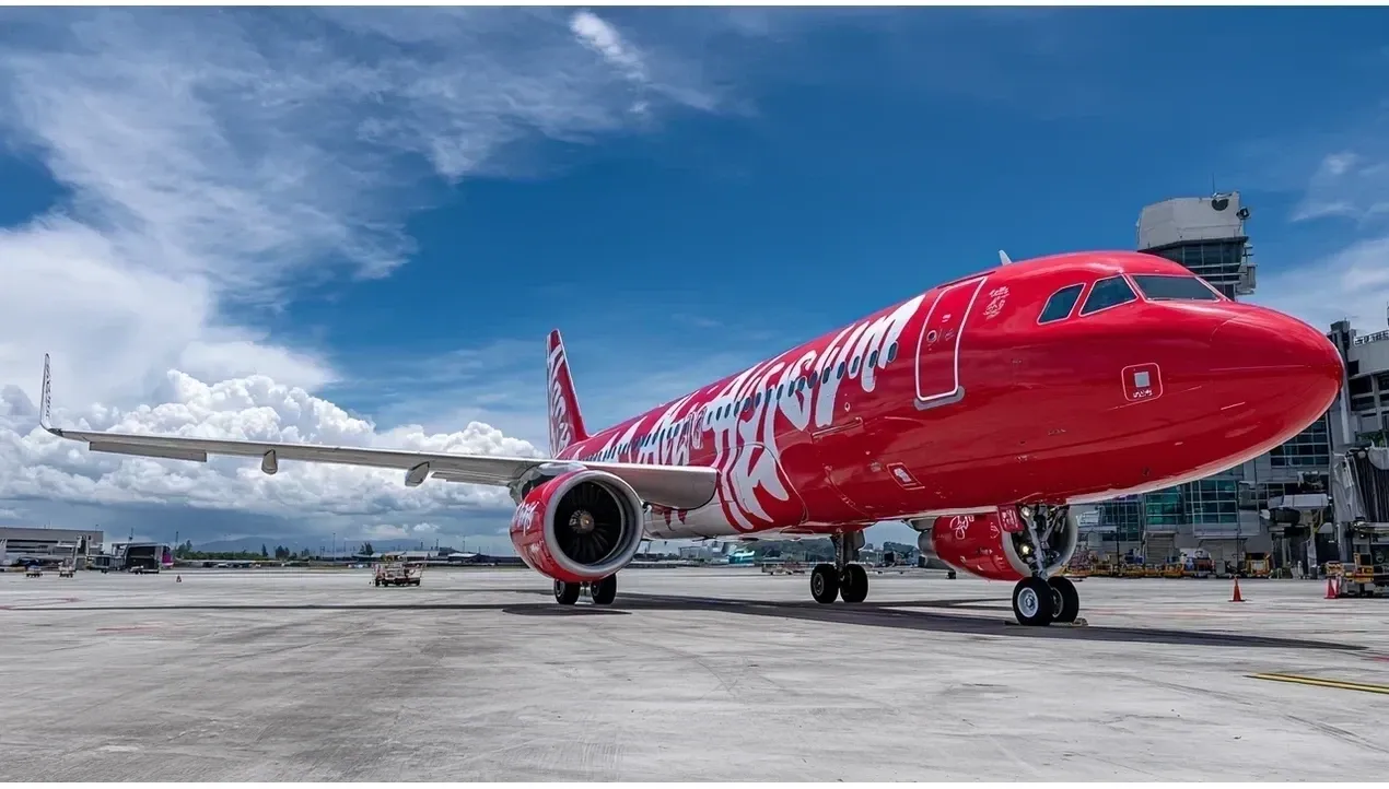 A vibrant red AirAsia aircraft dominates the frame showcasing its bold design against a cloudy sky and airport backdrop