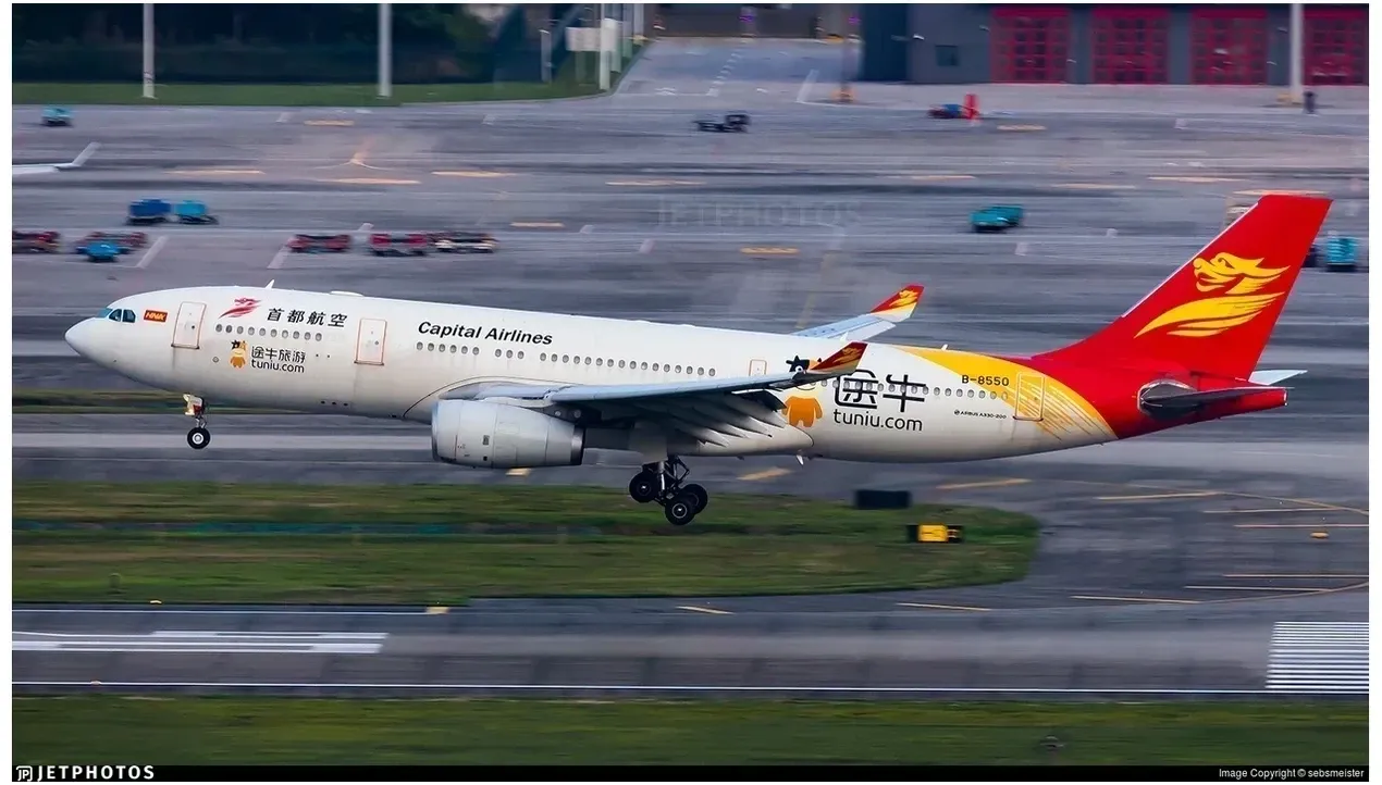 A Beijing Capital Airlines jet aircraft flies across the sky in motion its livery prominent against the blue expanse of the