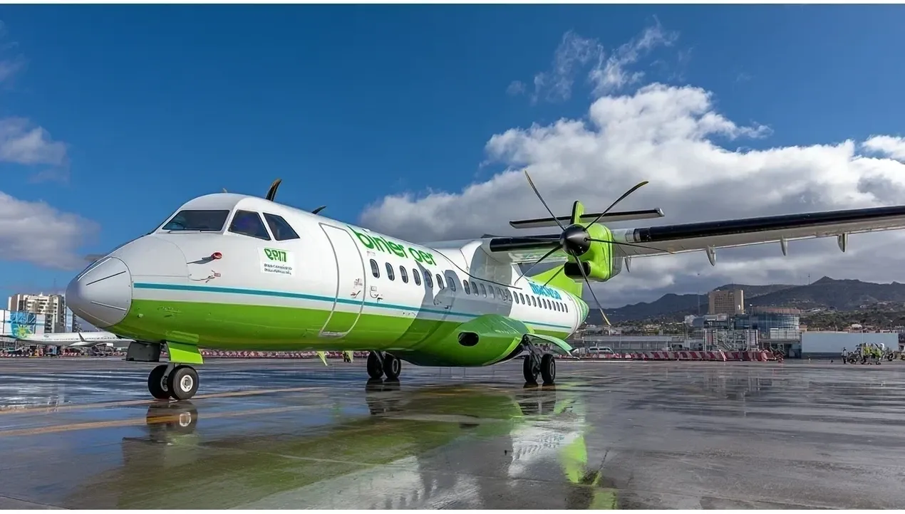 A vibrant Binter Canarias ATR 72 aircraft stands on the tarmac with wings extended reflecting the sky