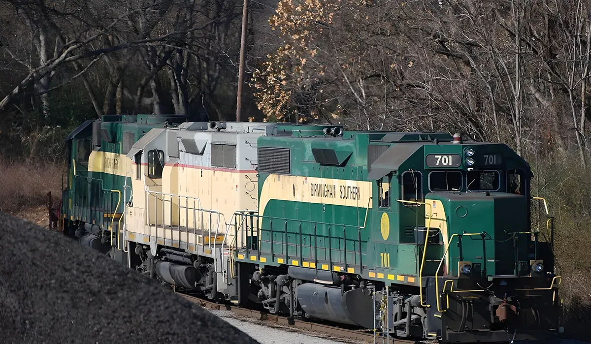 A green Birmingham Southern Railroad Company locomotive stands prominently on a track overlooking a hillside The train cars