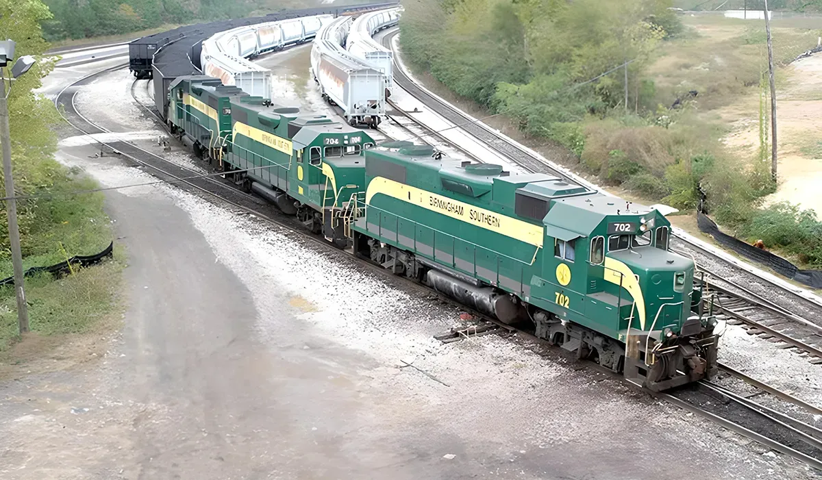 A freight train travels along a gravel track with a blurred background of trees and sky