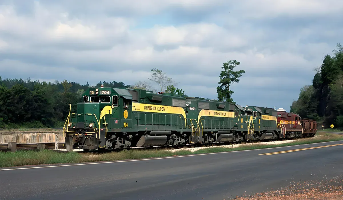 A vintage Birmingham Southern Railroad locomotive sits on a road alongside a grassy area with a utility pole and a yellow
