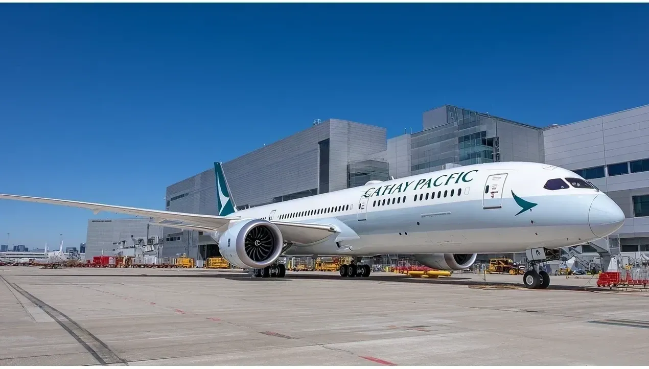 A Cathay Pacific Boeing 777 aircraft sits on the tarmac with service vehicles nearby at an airport