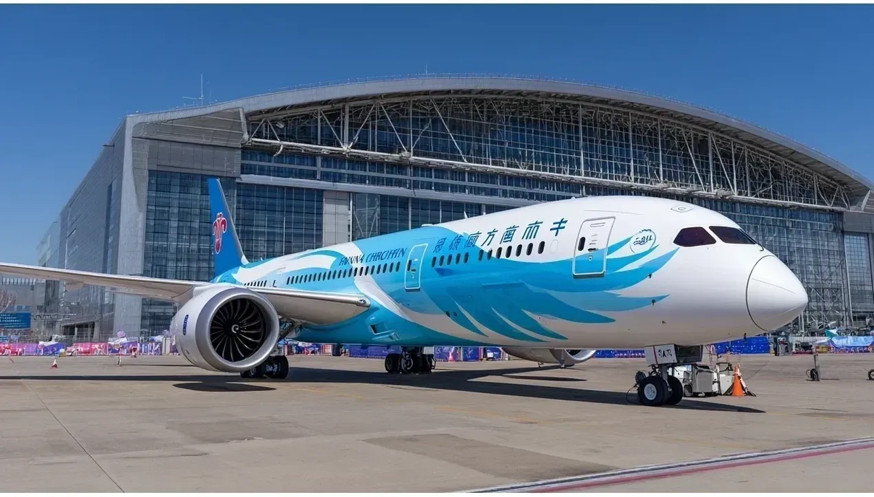 A China Southern Airlines Boeing 777 aircraft sits on a runway with a modern airport terminal in the background