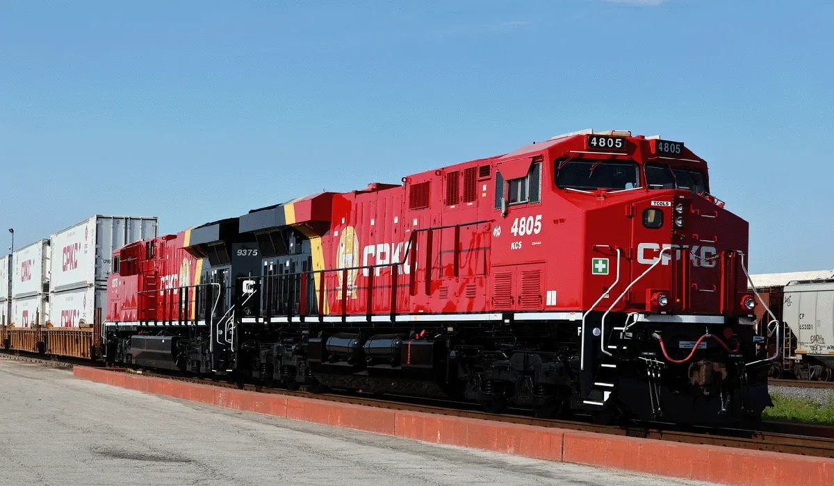 A red freight train car sits on a rail yard with containers in the background signifying efficient supply chain