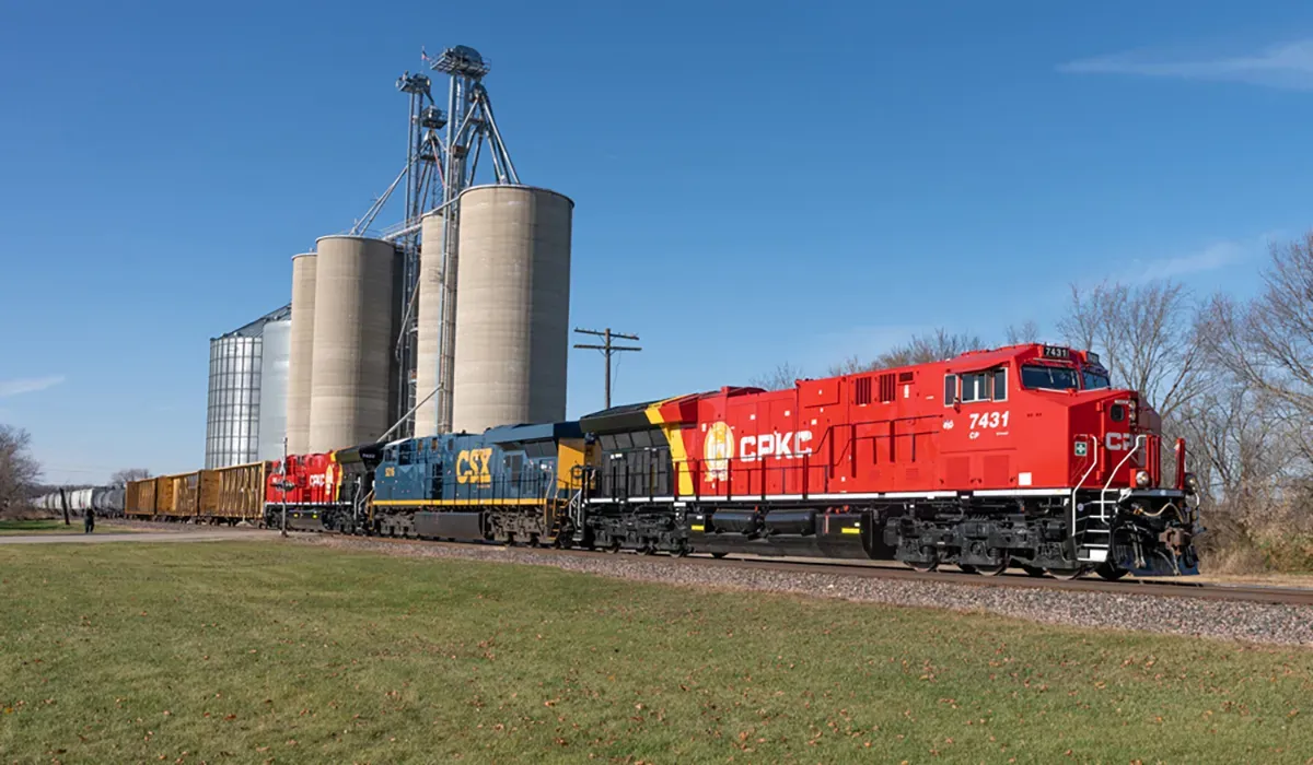 A bright red freight train stretches across a rural landscape with tall grain silos in the background The train appears to