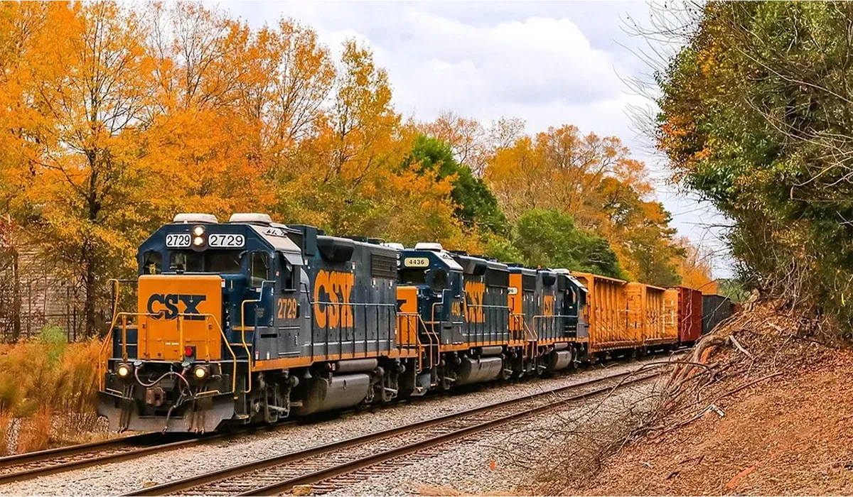 A CSX Transportation freight train travels along a railway track with a long freight car leading the train