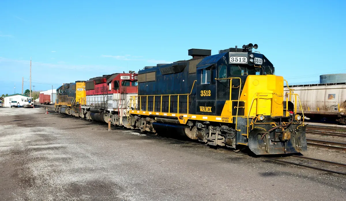 A large freight train with several cars sits on tracks in an industrial setting The train is primarily dark with yellow