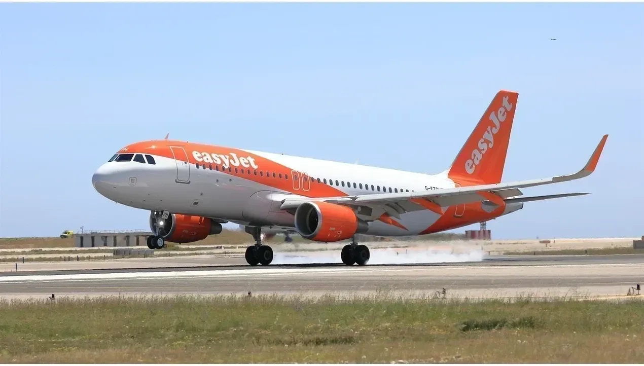 A bright orange easyJet aircraft taxis on the runway with a blue tail fin against a clear sky background