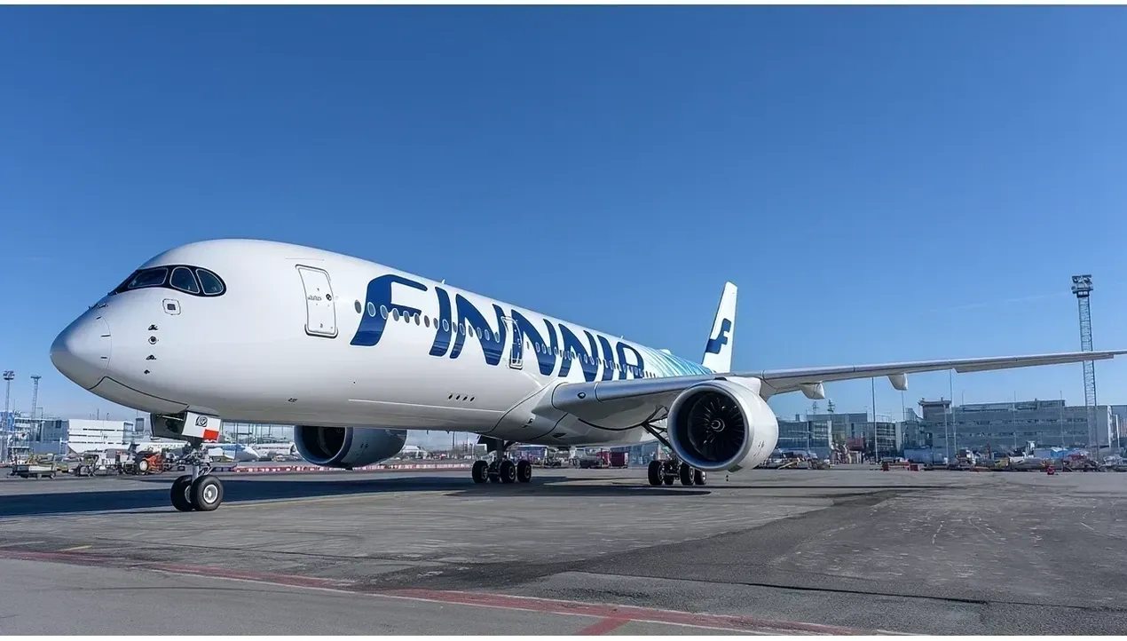 A Finnair Airbus A320 aircraft stands on the tarmac at an airport with baggage carts and airport infrastructure visible in