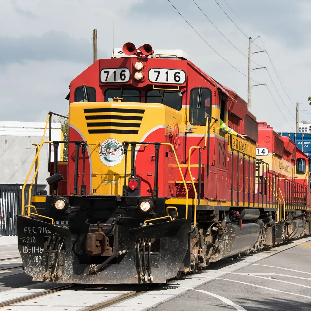 A Florida East Coast Railway freight train sits on a track with a prominent red and yellow locomotive The train appears to