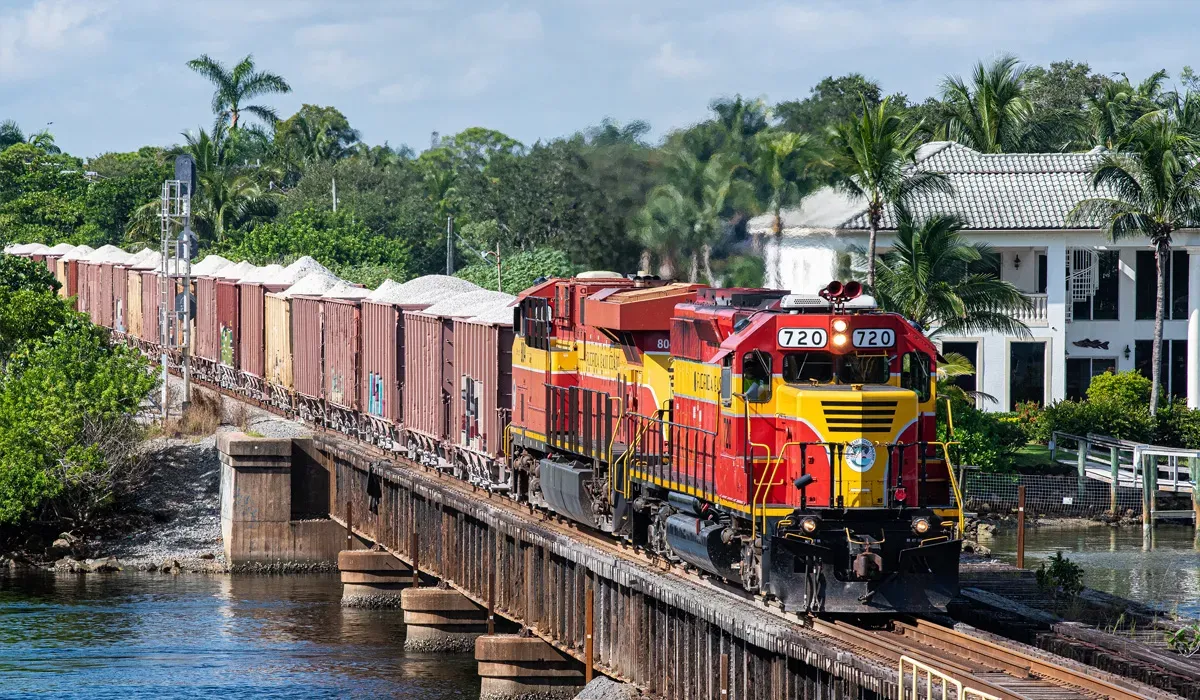 A freight train travels across a concrete railway bridge over a waterway in Florida The train is painted in the Florida East