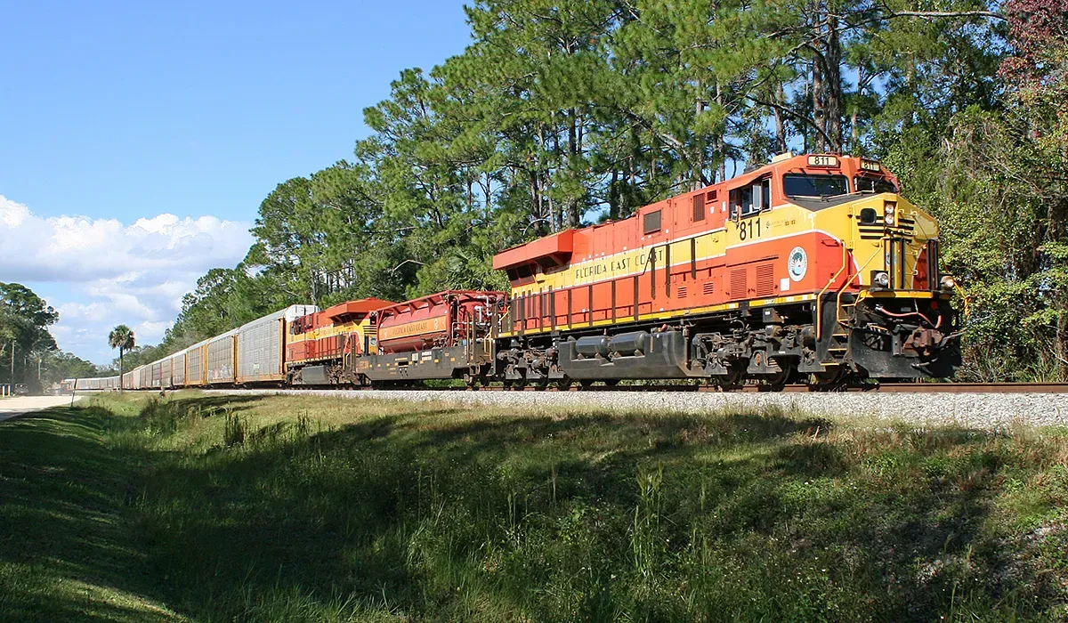 A Florida East Coast Railway locomotive identified as unit 811 travels along a sunny track surrounded by green vegetation