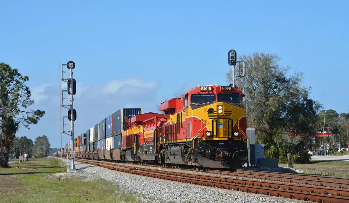 A long freight train travels along a sunny track in Florida The train is painted red and white and appears to be moving