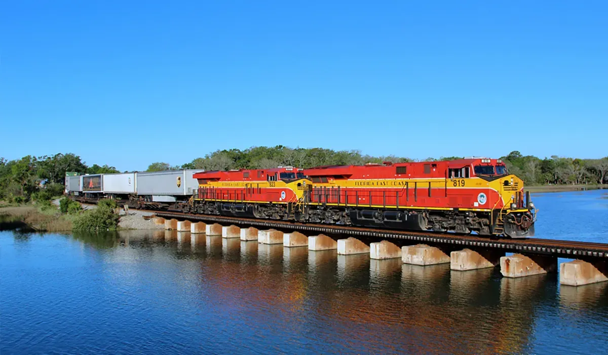 A Florida East Coast Railway train crosses a stone bridge over a calm waterway The train is a prominent red subject with