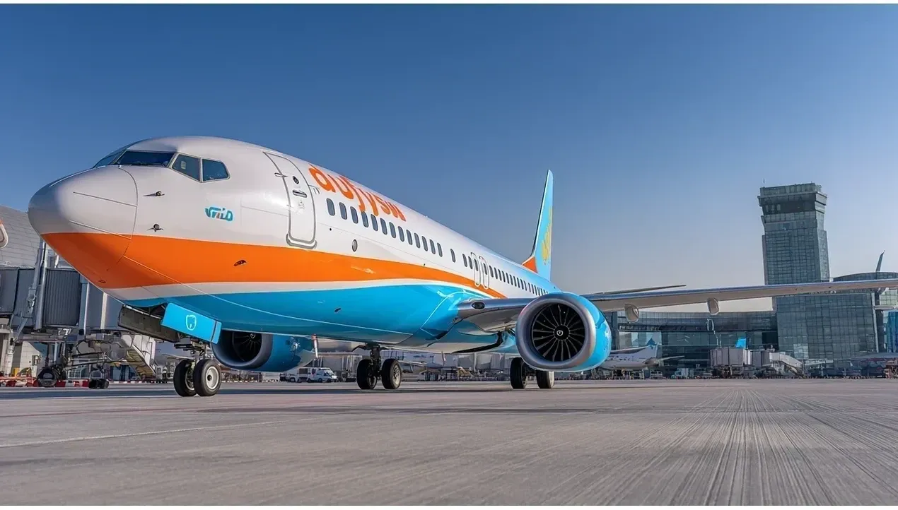 A bright blue and white flydubai aircraft sits on the tarmac awaiting departure surrounded by airport buildings