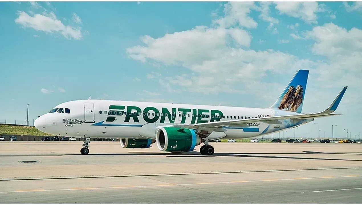 A white Frontier Airlines Boeing 737 aircraft sits on a runway with green engines and the airlines logo prominently displayed