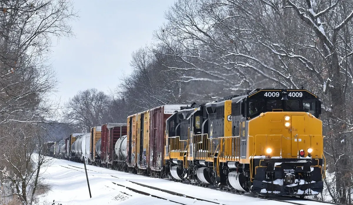 A yellow freight train with numerous cargo cars travels on a snowy track through a winter landscape highlighting efficient