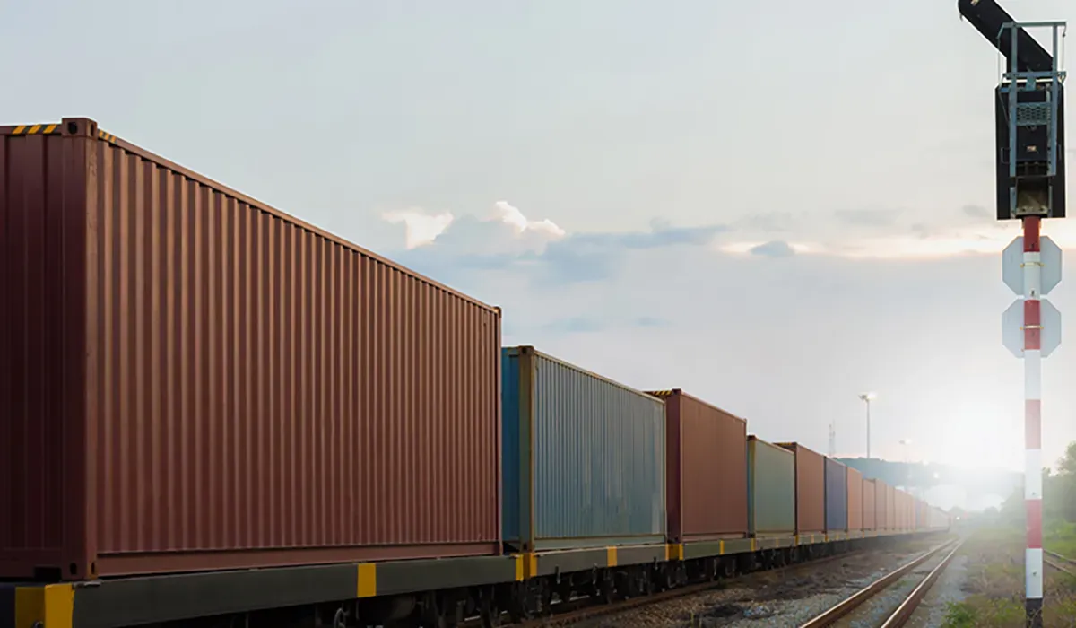 A long line of red freight cars stretches along a railway track under a bright sky The cars suggest efficient supply chain