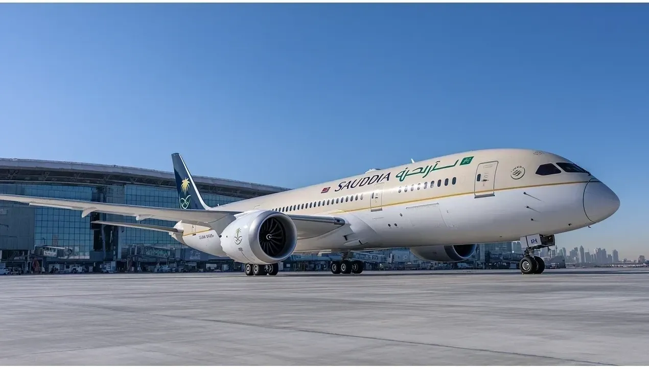 A Saudi Arabian Airlines Boeing 777 sits on the tarmac with prominent branding and engines ready for flight