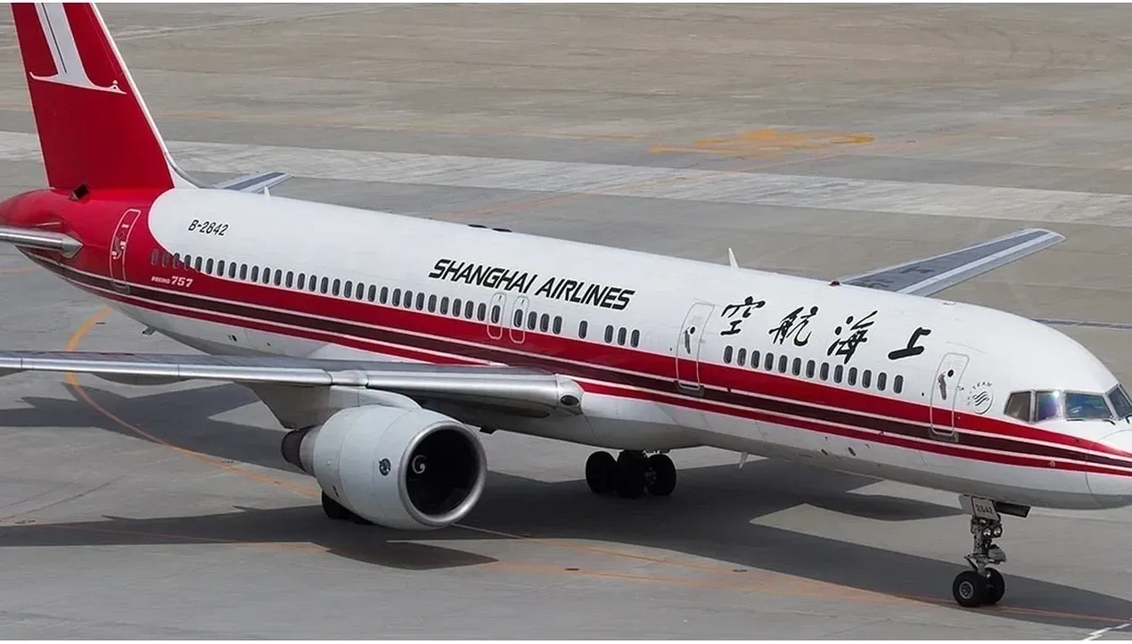 A Shanghai Airlines Boeing 757 aircraft stands on the tarmac with a prominent red tail and wings ready for flight detailed