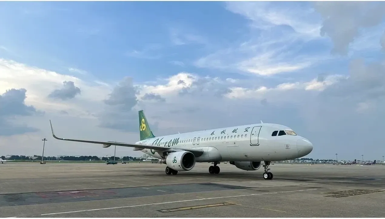 A white Spring Airlines aircraft sits on the tarmac a modern jet with green branding reflecting the skys soft hues