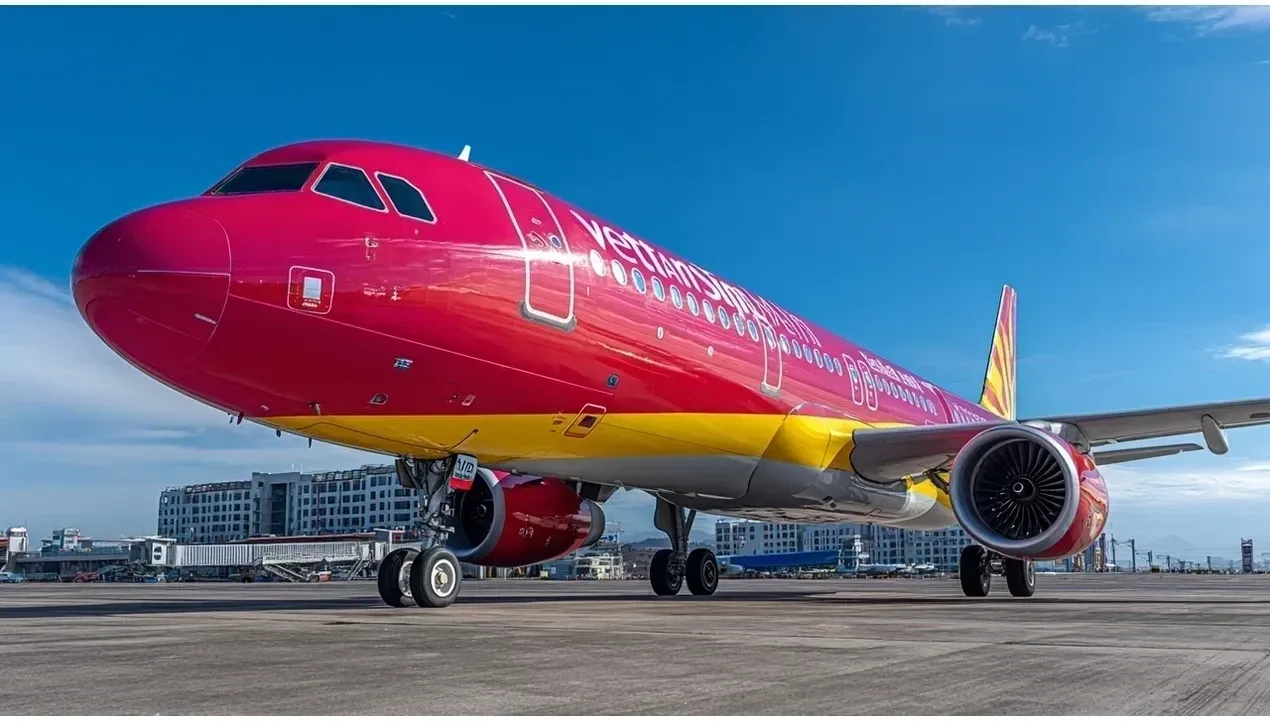 A vibrant red Vietjet Air aircraft sits on an airport tarmac against a backdrop of modern buildings Its powerful engines are