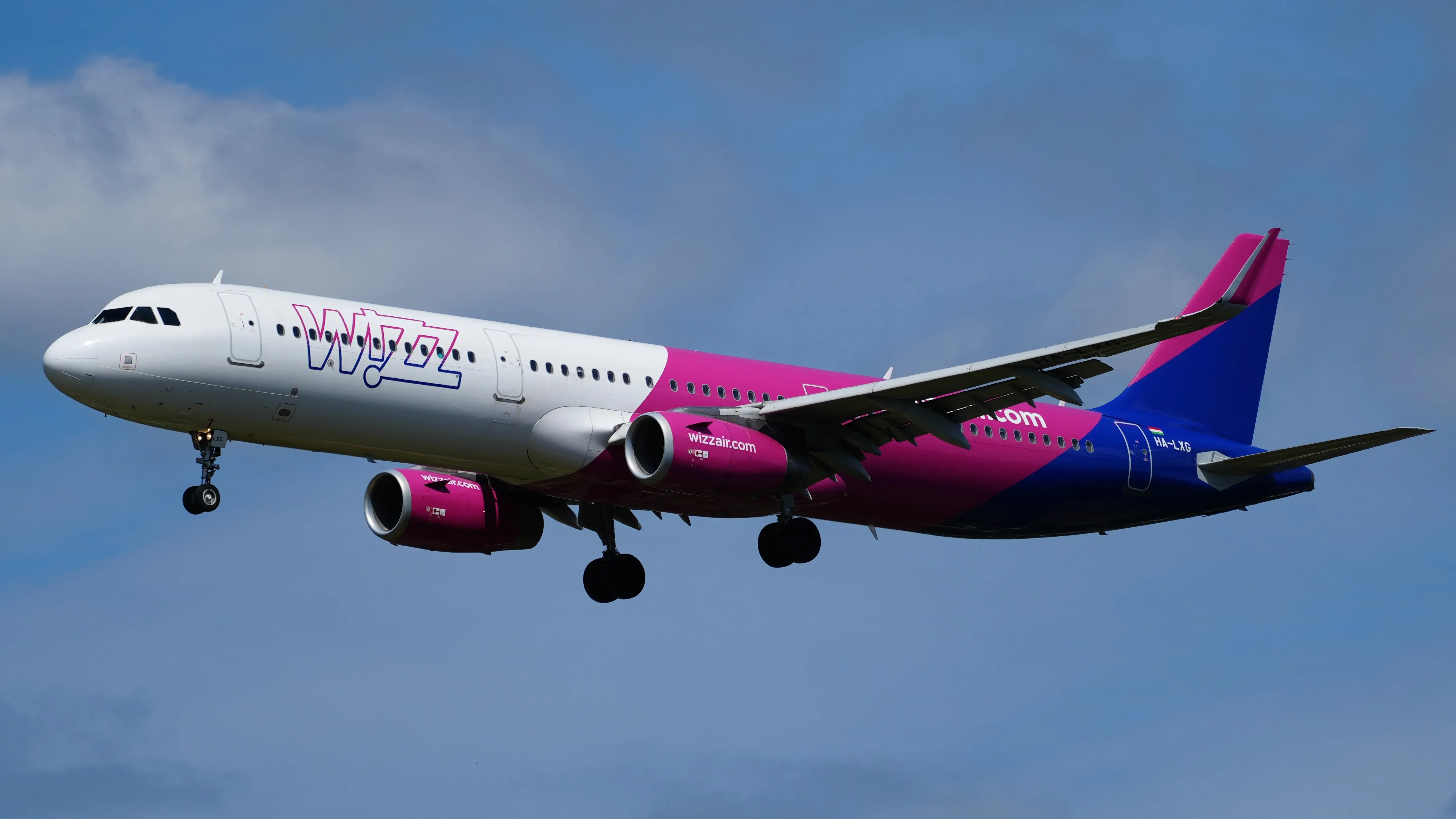 A bright wizz air aircraft dominates the frame with striking purple and white livery soaring against a blue sky