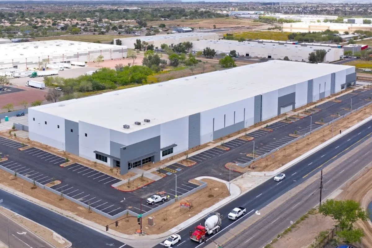 A large modern warehouse complex dominates the view with expansive gray roofs and a paved access road A concrete truck is