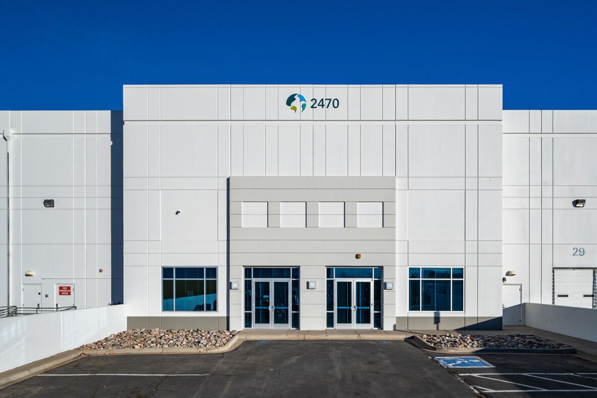 A modern white building with double doors sits on a paved surface surrounded by rock landscaping