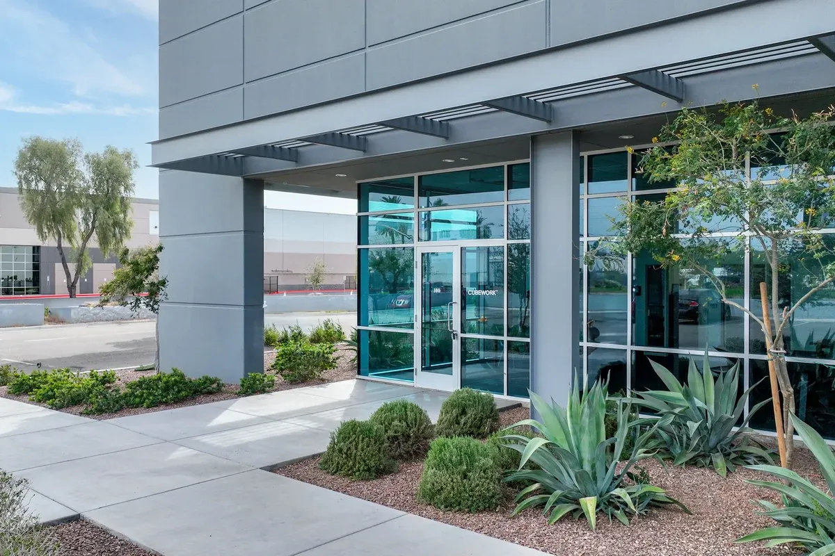 A modern building facade features a glass entrance set among lowlying shrubs and succulents A concrete walkway leads to the
