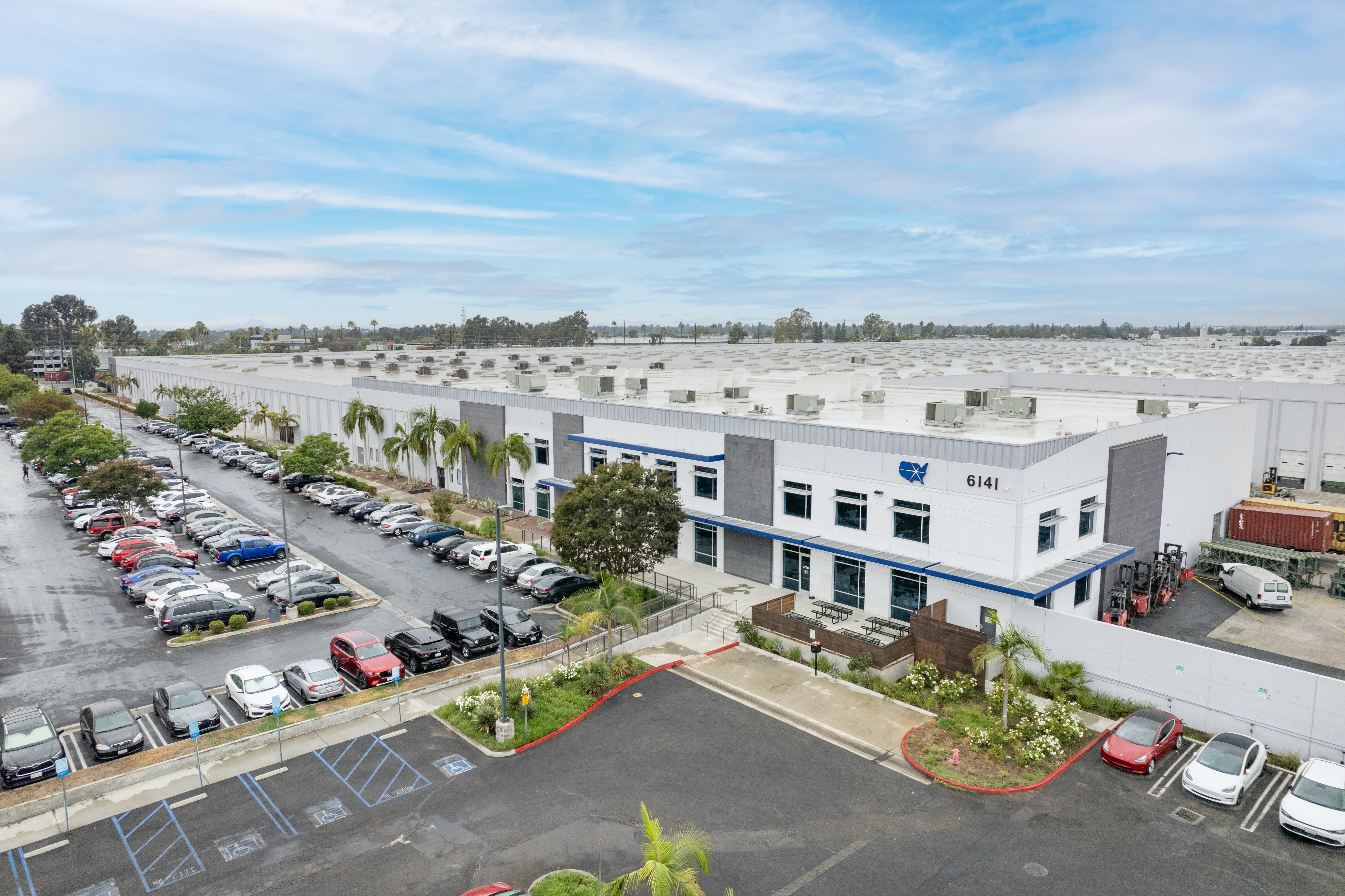 Modern industrial buildings with blue accents and landscaping are pictured A concrete parking lot extends into the view