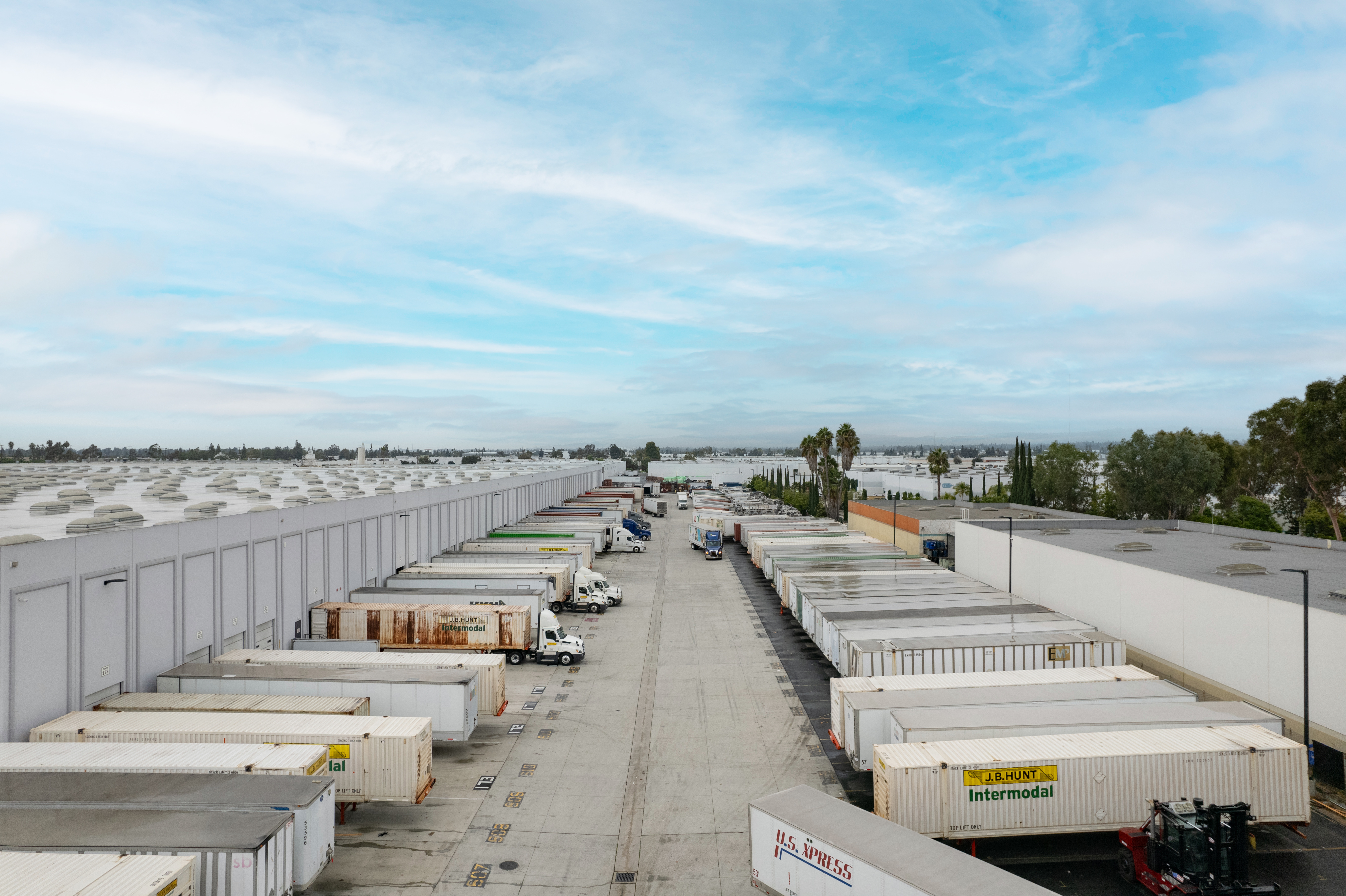 A long warehouse with rows of stacked shipping containers dominates the scene under a clear sky