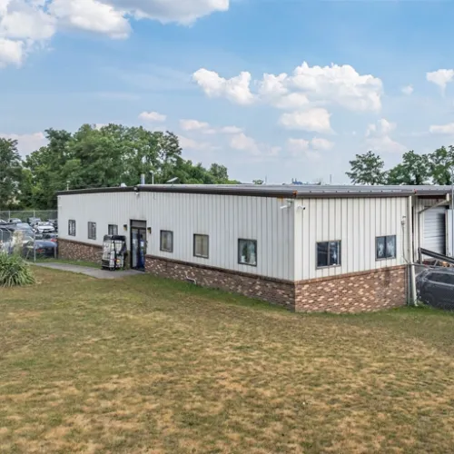 Single-story commercial building with gray metal siding, brick base, multiple windows, and surrounding lawn area.