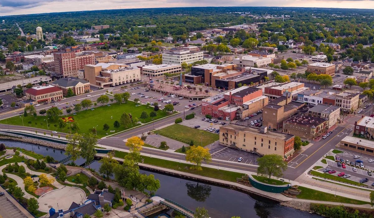 An aerial view of Elkhart Indiana shows a cityscape dominated by buildings along a riverfront street A green park area is